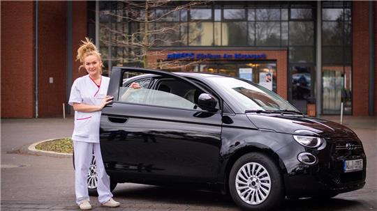 Künftigen Krankenpflegekräften wird ein Dienstfahrzeug bei Anstellung geboten. Im Bild: Krankenpflegekraft Marina Popov mit dem Elektroauto Fiat 500. Foto: Arnd Hartmann