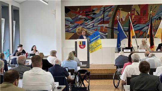 Landrat Kai Seefried stellt das Projekt in einer Kreistagssitzung vor. Er zeigt eine von ukrainischen Frontsoldaten unterschriebene Flagge, die ihm als Dankeschön für die Hilfstransporte überreicht worden war.