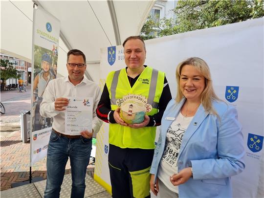 Landrat Kai Seefried und Stades stellvertretende Bürgermeisterin Melanie Rost-Reinecke nehmen Tobias Archut vom Allgemeinen Deutschen Fahrradclub in ihre Mitte. Foto: Landkreis Stade