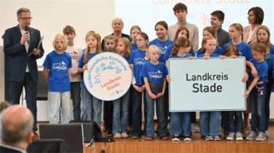 Landrat Kai Seefried und die Buxtehuder Stieglitze präsentieren das Siegel „Kinderfreundliche Kommune“ für den Landkreis Stade.