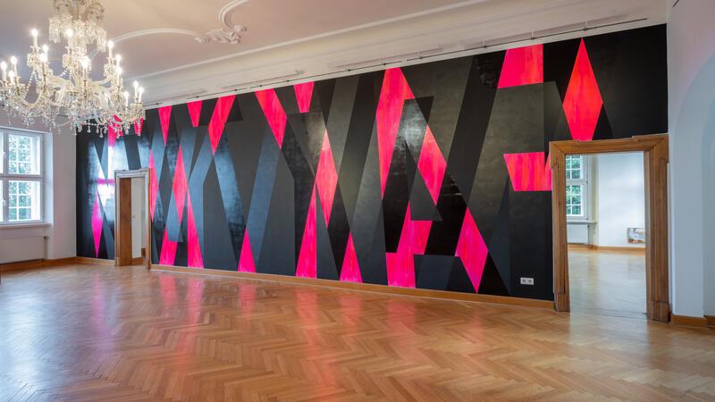 Die lange Wand des großen Schlossraums zieren die Worte Faktum und Fiktion als gegeneinanderlaufende Schriftzüge 