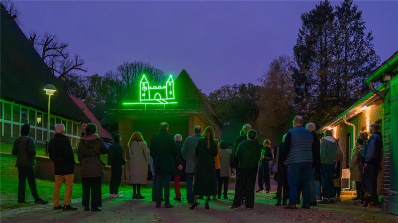 Feierliche Einweihung der grün leuchtenden Schloss-Skizze auf dem einstigen Pferdewaschhaus, mit einer Schar von Gästen in der Abenddämmerung