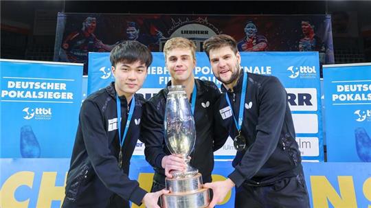 Lin Yun-ju (l-r), Truls Moregardh und Dimitrij Ovtcharov, alle von TTC Neu-Ulm, jubeln mit dem Champions-League-Pokal. In der Bundesliga spielt der Verein nicht mehr mit.