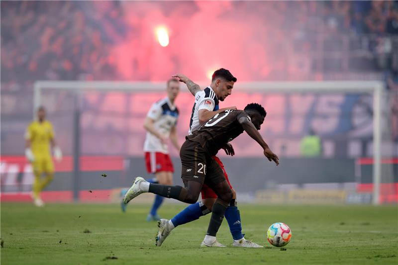 HSV feiert Sieg in aufregendem Stadtderby Ludovit Reis vom Hamburger SV (hinten) attackiert Afeez Aremu vom FC St. Pauli. Im Hintergrund haben HSV-Fans Pyrotechnik gezündet. Foto: Christian Charisius/dpa