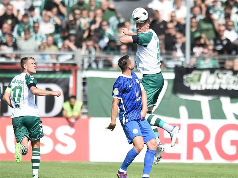 Lübecks Jannik Löhden überspringt im Kopfballduell Rostocks John Verhoek. Das Erstrundenspiel im DFB-Pokal hat der Regionalligist VfB Lübeck gegen den Zweitligisten Hansa Rostock mit 1:0 gewonnen. Foto: Michael Schwartz/dpa