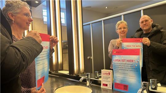 „Luisa ist hier!“: Gleichstellungsbeauftragte Hiltrud Gold und Sicherheitschef Torsten Lüders bewerben das neue Hilfsangebot mit Plakaten in den Damentoiletten des Musikladens.