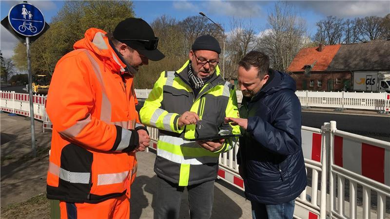 Lukas Wiener (Bauüberwachung), Thomas Meinefeld (Contur) und Michael Krüger (Gemeinde Düdenbüttel, von links) schauen sich auf dem Tablet an, wie es mit der Ortsdurchfahrt Düdenbüttel weitergeht.