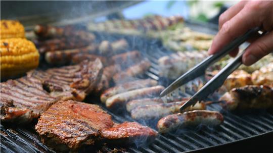 Maiskolben, Fleischspieße, Bratwürste und Steaks liegen auf dem Rost eines Gasgrills. 