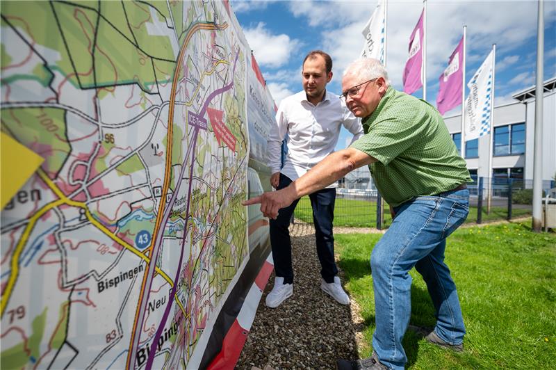 Malte Schmidt (l), Geschäftsführer vom Ralf Schumacher Cart Center und Stephan Müller (r), Bürgerinitiative (BI) Unsynn, blicken auf einen Banner mit einem möglichen Verlauf einer Bahntrasse. Foto: Philipp Schulze/dpa