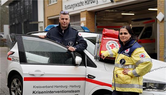 Malte Stüben, Sozialpädagoge und Teamleiter des Kriseninterventionsteams (KIT) des Deutschen Roten Kreuzes (DRK), und Nina Satya Paulsen, Psychologin und psychiatrische Psychotherapeutin, stehen an ihrem Einsatzfahrzeug auf dem Gelände des DRK-Kreisverbands Hamburg-Harburg e. V. Foto: Marcus Brandt/dpa