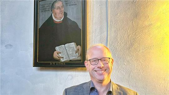 Marc Wischnowsky vor einem Porträt Martin Luthers in St. Cosmae in Stade.
