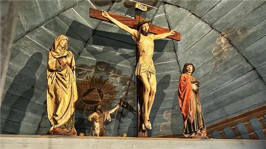 Maria, Jesus am Kreuz und der Apostel Johannes bilden die Kreuzigungsgruppe in der Borsteler Kirche. Direkt dahinter ist Jesu Auferstehung zu sehen.