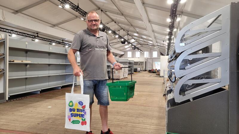 Marktleiter Peter Kross präsentiert die Mehrwegtaschen mit dem Superstore-Logo.