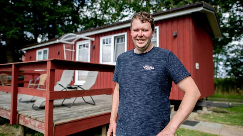 Markus Mushardt, Landwirt und Betreiber eines Ferienhofs, steht vor einem Tiny House aus Holz.