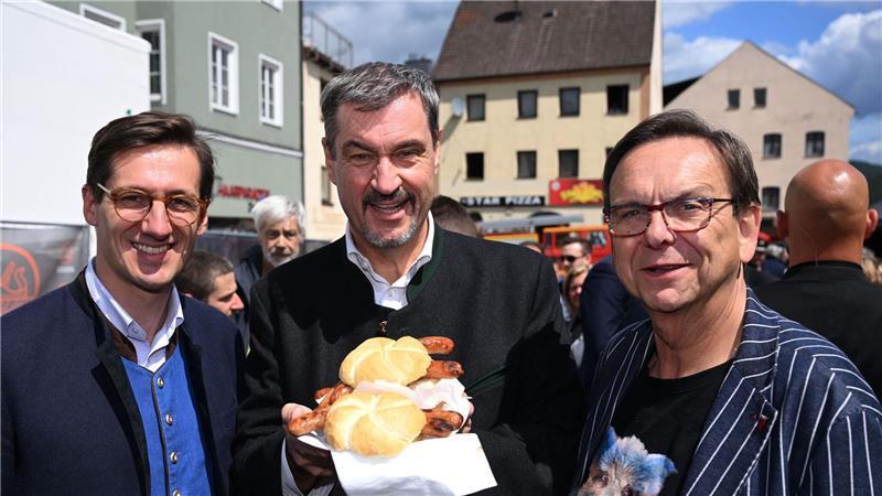 Schweine-Wettgrillen mit Söder und Peta-Protest Markus Söder (M.) hält Bratwurst-Semmeln in die Kamera.