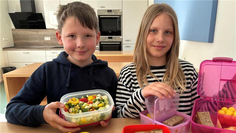 Marlon Uhl und Laura Weddemann zeigen ihre Brotdosen. Die Grundschüler haben Wurstbrot, Obst und Salat, aber auch etwas Süßes dabei.