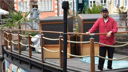 Künstler Martin Karl Kufieta steht oben an Deck des bunt bemalten Kunstkudders an der Reling