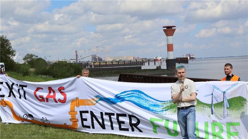 Nein zu LNG: Klimacamp auf einer Obstplantage in Guderhandviertel Martin Lüdders, aktiv in der Grünen Jugend und im Klimabündnis gegen LNG im Kreis Stade, redet am Dienstag bei der Demo. im Hintergrund ist das LNG-Terminal in Stade zu sehen.