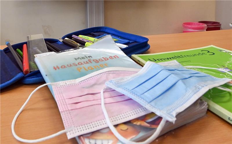 Masken liegen während einer Pause auf Arbeitsmaterialien eines Schülers in einem Klassenraum einer Grundschule. Foto: Patrick Pleul/dpa-Zentralbild/dpa