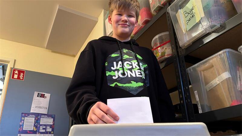 Max (11) wirft stolz seinen Stimmzettel in die Wahlurne ein.