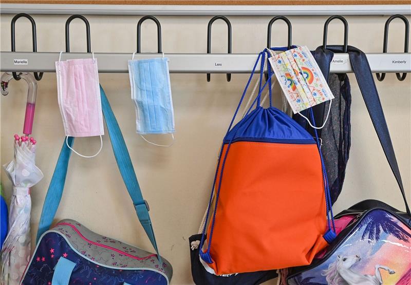 Medizinische Masken und Schultaschen hängen in einer Schulgarderobe.