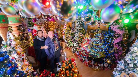 Mehr Weihnachten geht kaum: Susanne und Thomas Jeromin stehen inmitten von Weihnachtsbäumen im Wohnzimmer ihres Hauses.