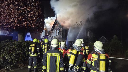 Mehrere Einsatzkräfte der Feuerwehr vor dem brennenden Gebäude.