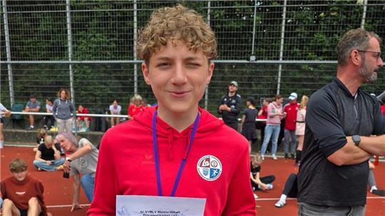 Elias Frank steht auf einer Tartanbahn, trägt einen roten Pullover, eine Medaille um den Hals,l ächelt und zeigt seine Siegerurkunde.