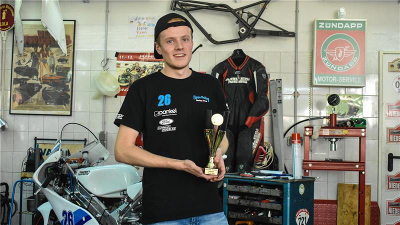 Jan Drewes hält einen Pokal in seiner Werkstatt in der Hand.