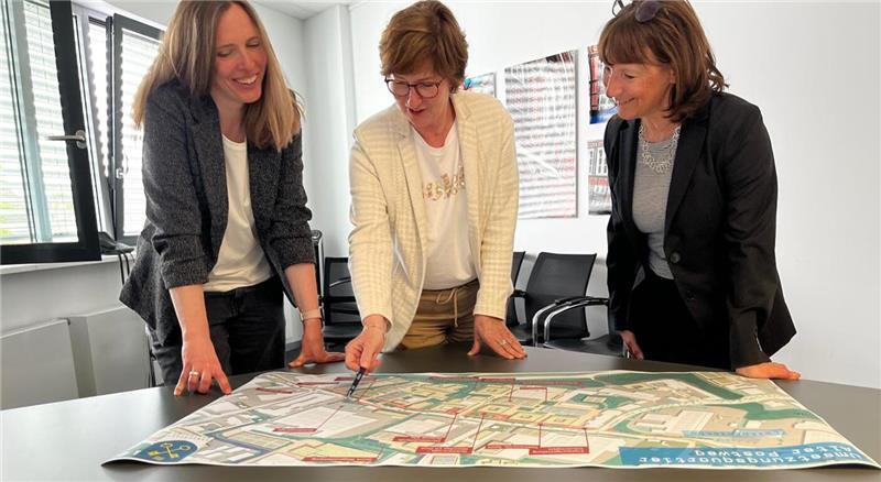 Melanie Mierau und Kerstin Maack von der Wirtschaftsförderung und Bürgermeisterin Katja Oldenburg-Schmidt schauen sich die Vision des Gewerbegebiets Alter Postweg an.