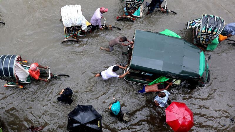 Menschen bewegen sich mühsam durch das Hochwasser in der Stadt Chittagon.