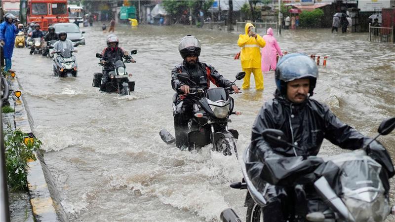 Menschen fahren bei starkem Regen in Mumbai mit Motorrädern durch eine überschwemmte Straße.