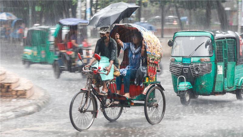 Menschen fahren im Monsunregen durch eine belebte Straße in Dhaka in Bangladesch.