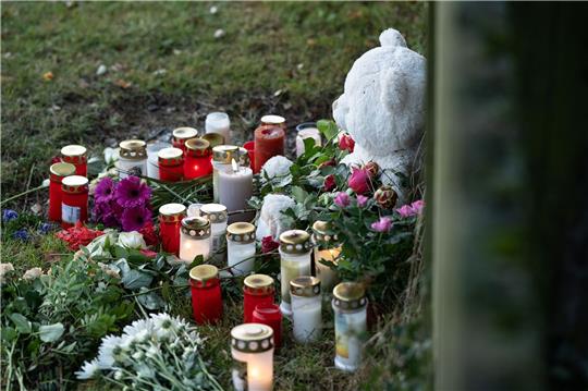 Menschen haben Kerzen, Blumen und ein Stofftier in Gedenken an die tote 14-Jährige vor einen Zaun gelegt.