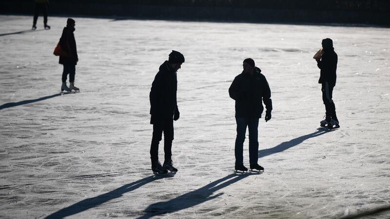 Menschen laufen auf auf einem zugefrorenen Stadtteich, Schlittschuh.