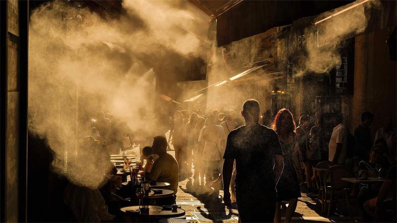 Menschen laufen unter Sprinklern eine Straße in Nizza entlang während einer Hitzewelle an der französischen Riviera.