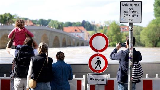 Menschen schauen sich in der Altstadt am Donauufer hinter einer Schutzwand das Hochwasser an.