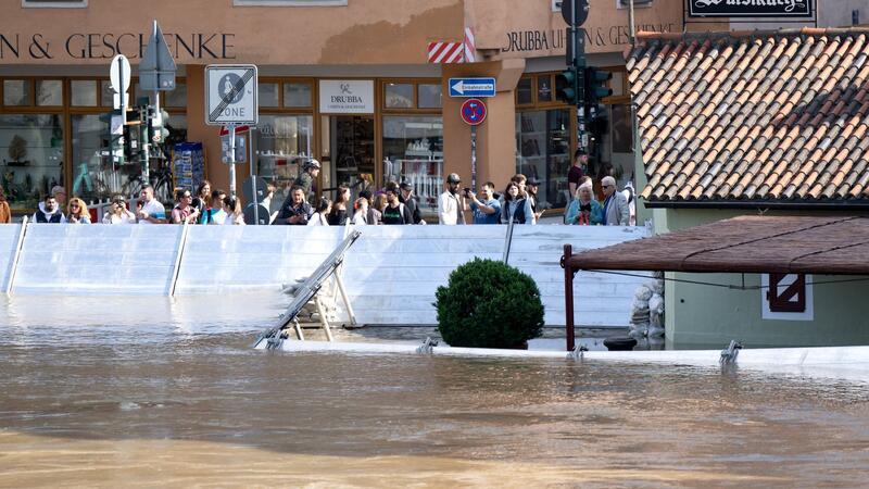 Menschen schauen sich in der Altstadt von Regensburg hinter einer Schutzwand das Hochwasser an.