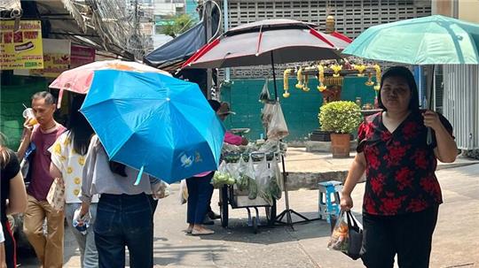 Menschen schützen sich in Bangkok mit Schirmen vor der extremen Hitze und vor der Sonne.