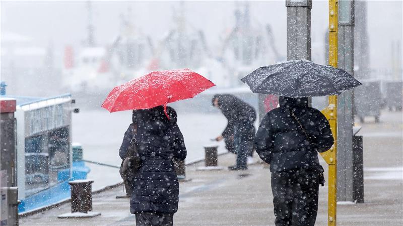Menschen schützen sich vor Schneefall mit Regenschirmen bei einem Spaziergang an den Landungsbrücken am Hamburger Hafen.