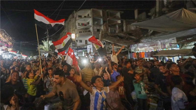 Menschen schwenke agyptische Flaggen und verfolgen im zentralen Gazastreifen das WM-Spiel Ägypten gegen Belgien auf einer Großbildleinwand.