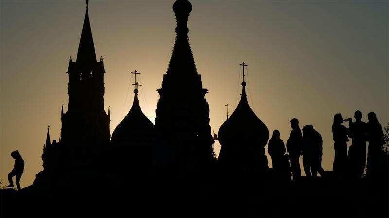 Menschen spazieren bei Sonnenuntergang im Zaryadye-Park in Moskau vor dem Hintergrund des Spasskaja-Turms des Kremls und der Basilius-Kathedrale.