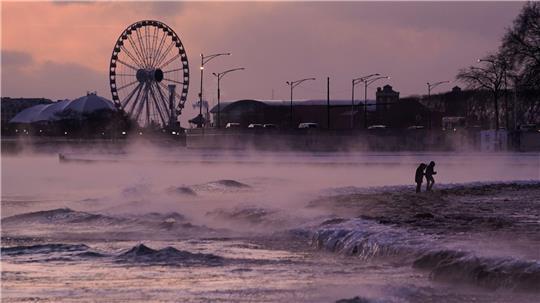 Menschen spazieren in Chicago über einen mit Eis bedeckten Strand am Ufer des Michigansees.