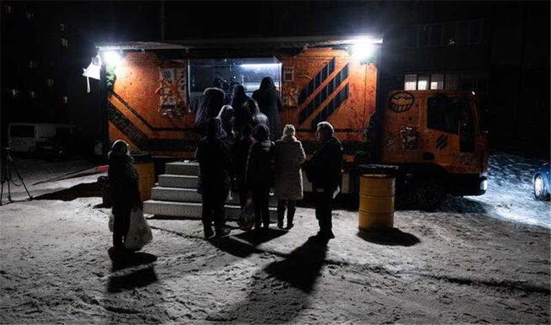 Menschen stehen Schlange vor einem Verpflegungswagen der ukrainischen Streitkräfte, um in einem Wohnviertel kostenlos warme Mahlzeiten für Menschen zu erhalten, die nach wiederholten russischen Luftangriffen auf den Energiesektor des Landes ohne Strom in ihren Häusern sind.