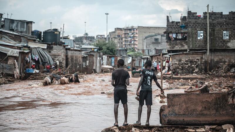 Menschen stehen am Ufer eines überfluteten Flusses in den Mathare-Slums in Nairobi.