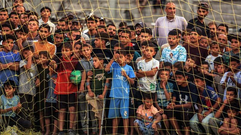 Menschen verfolgen ein Fußballspiel zwischen einer Mannschaft aus Gaza gegen eine Mannschaft aus Chan Yunis auf einem Gelände zwischen Zelten, in denen Binnenflüchtlinge untergebracht sind.