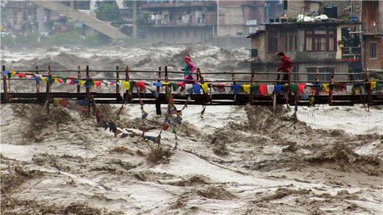 Menschen wagen im nordindischen Bundesstaat Himachal Pradesh trotz schwerer Überschwemmungen den Weg über eine Brücke, um den Fluss Beas zu überqueren.