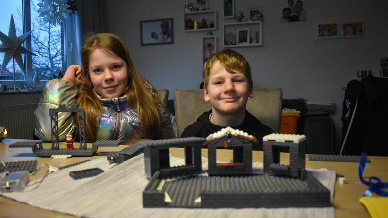 Miriam und Linus Patjens sitzen an einem Tisch. Vor ihnen steht ein unfertiger Weihnachtsmarkt aus Lego.