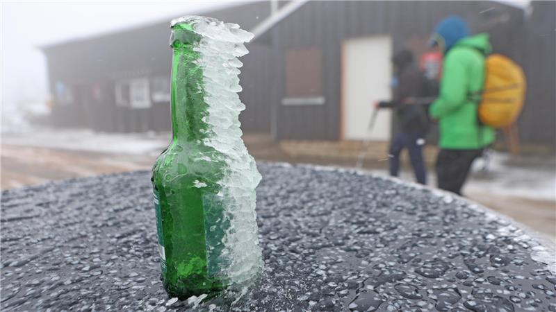 Mit Eis bedeckt ist eine Glasflasche auf einem Tisch auf dem Brocken. 