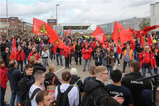 Mit Fahnen der Gewerkschaft IG Metall stehen Beschäftigte bei einem Warnstreik während einer Kundgebung vor dem Werksgelände von Airbus.